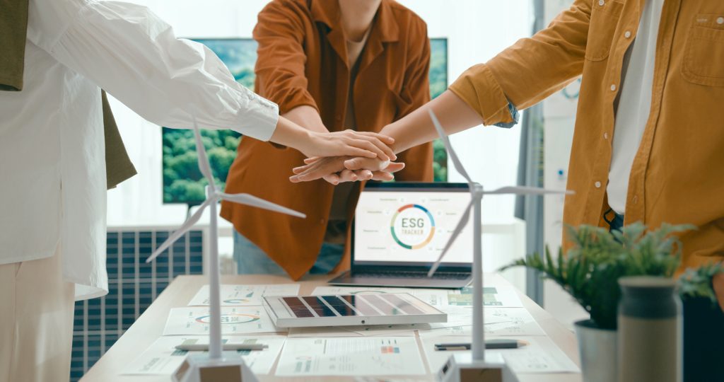 Diverse team unites hands over desk with renewable energy models, symbolizing cooperation and agreement on sustainable business practices.Eco-Friendly Business Team Discussing ESG Goals.